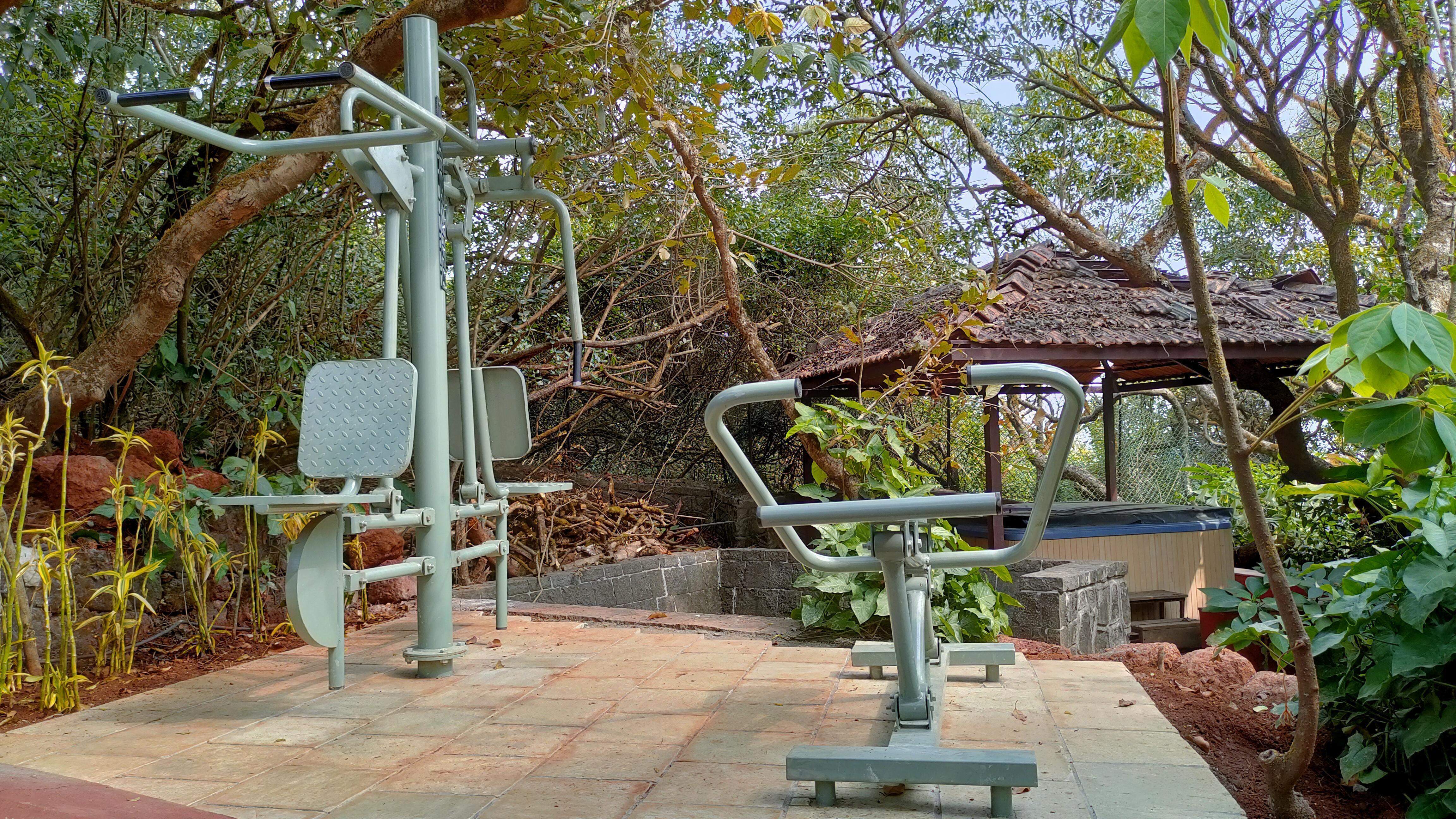 A well-shaded outdoor fitness zone at Ramsukh Resort, set amidst greenery, featuring exercise machines for physical activity in a natural setting.